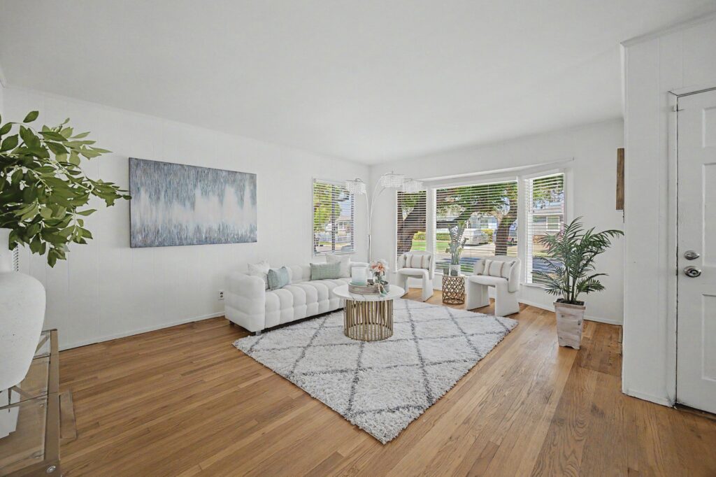Wide view of a staged living room with white furnishings and hardwood floors